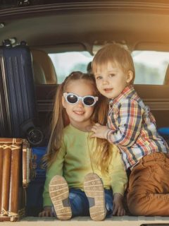 boy and girl in back of vehicle with suitcases