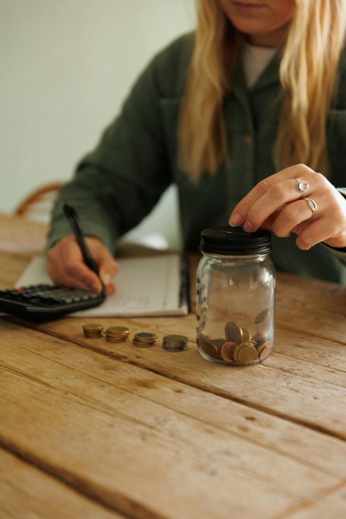woman with calculator and notebook adding change to a jar