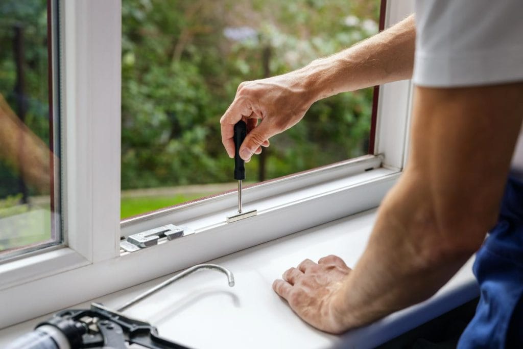 man using screwdriver on window pane