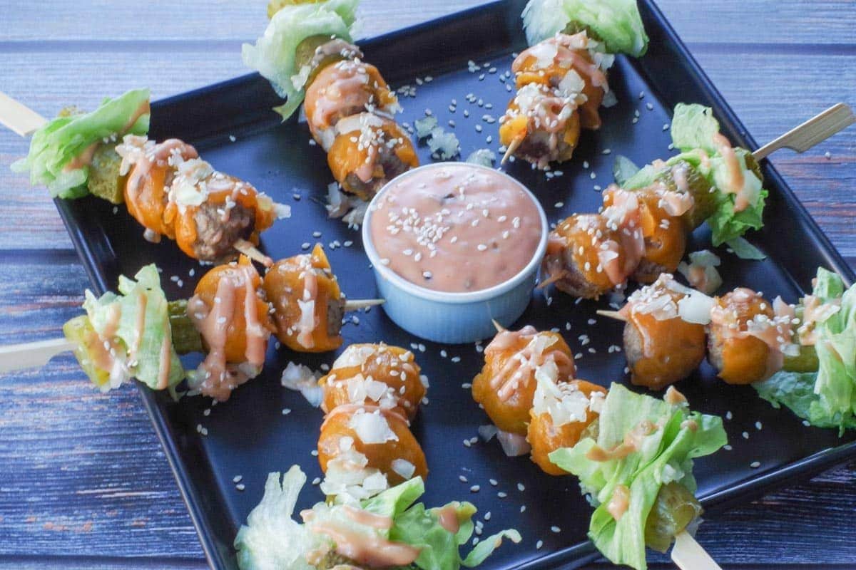 Skewers of cheesy beef bites with sauce in a bowl.