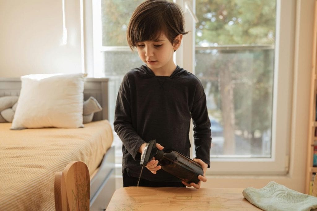 little boy spraying cleaner on wooden table