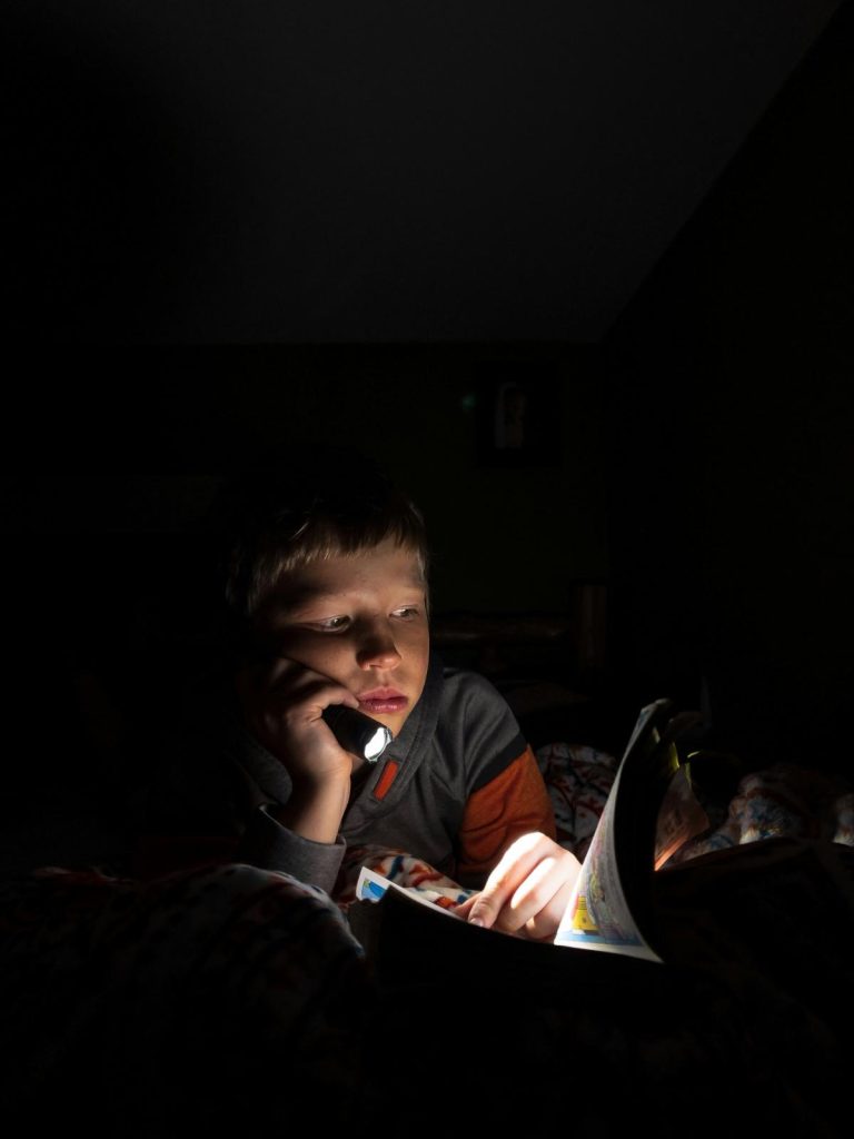 boy with flashlight reading comic book in the dark