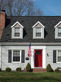 a cape cod style home with red door and flag out front