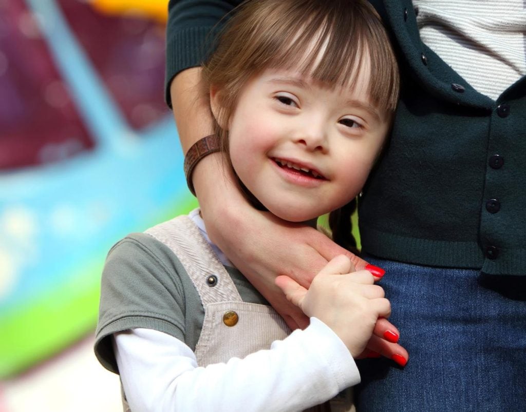 smiling girl with downs syndrome holding mother's hand