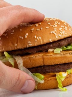 man's hand reaching for a double cheeseburger with lettuce onions and mac sauce