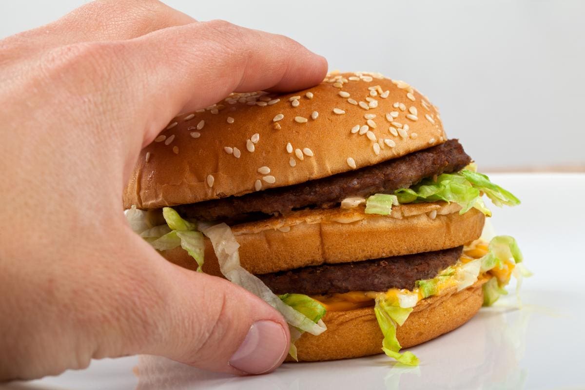 man's hand reaching for a double cheeseburger with lettuce onions and mac sauce