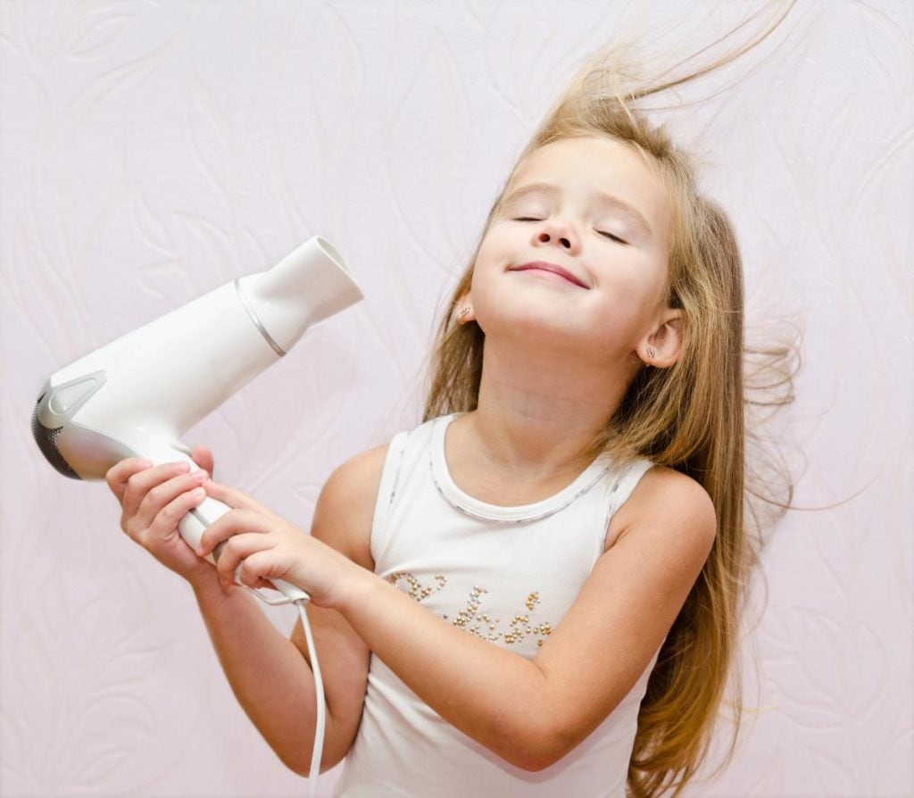 smiling blonde girl using a hair dryer