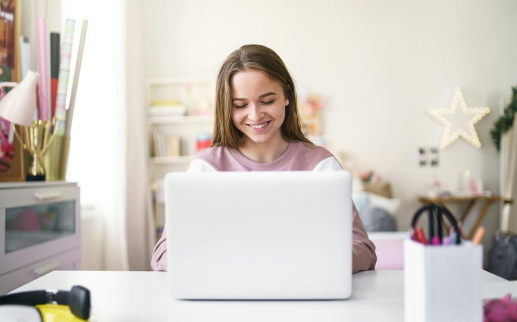 smiling teen girl using white laptop