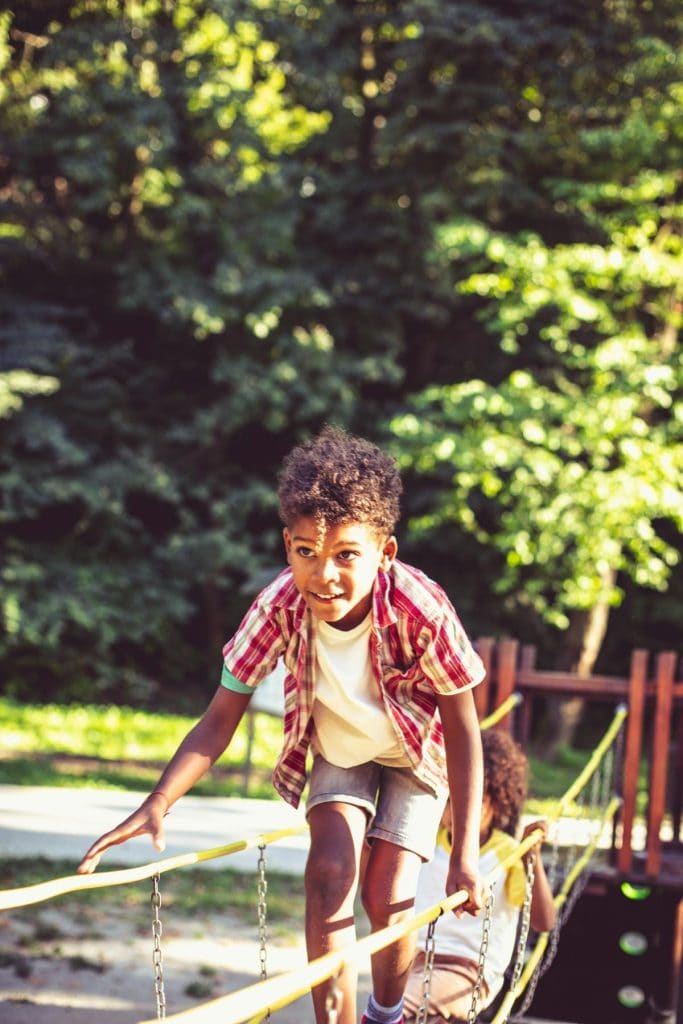 boy walking across swinging bridge on playground equipment