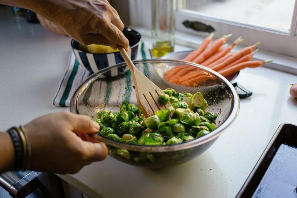 man tossing brussels sprouts in a bowl with oil and seasonings