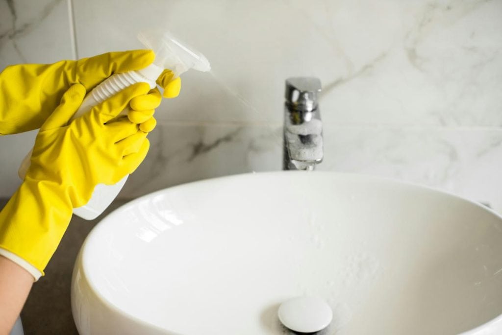 spraying cleaner on bathroom sink faucet