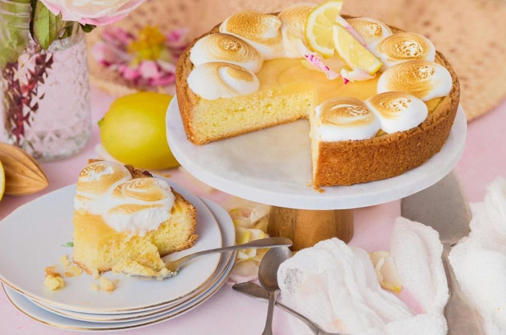 closeup shots of a lemon meringue cake on a stand with a slice of the cake to the left on a white plate