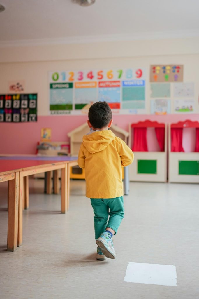 small boy in rain jacket walking through classroom