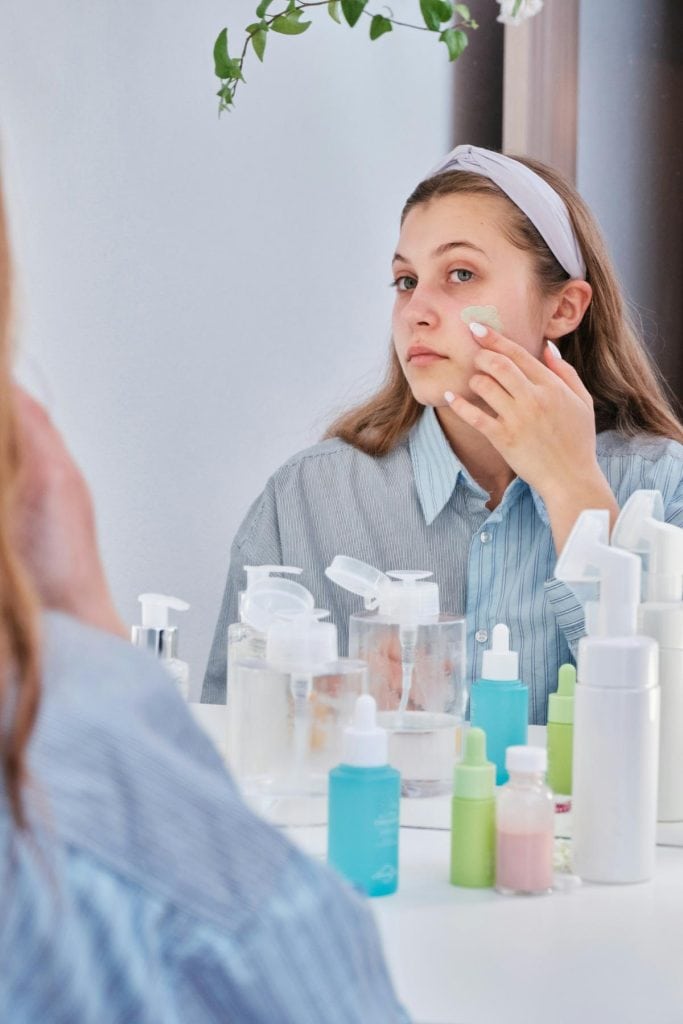 woman using skincare products in front of mirror