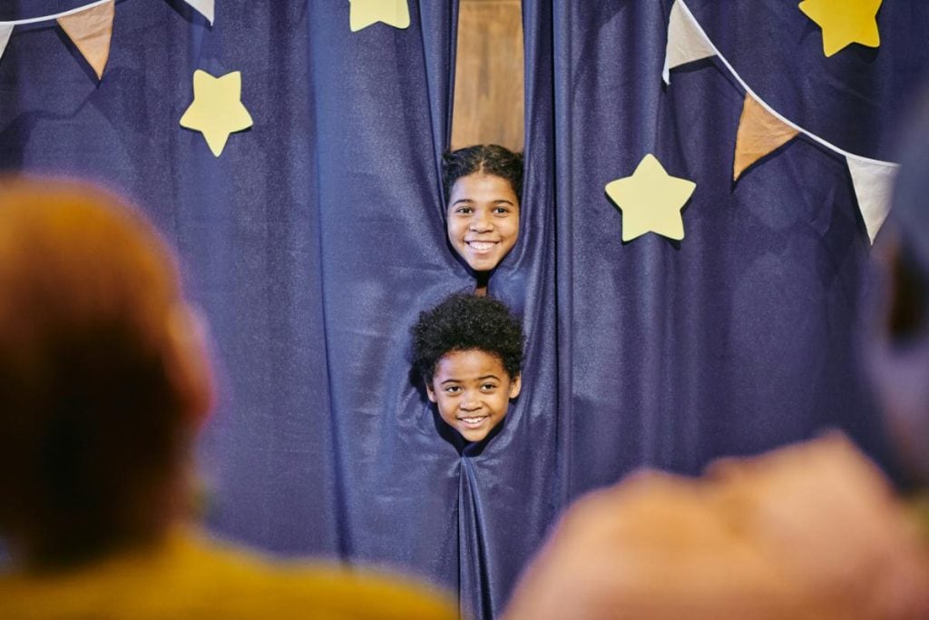 kids peeking from behind a stage curtain