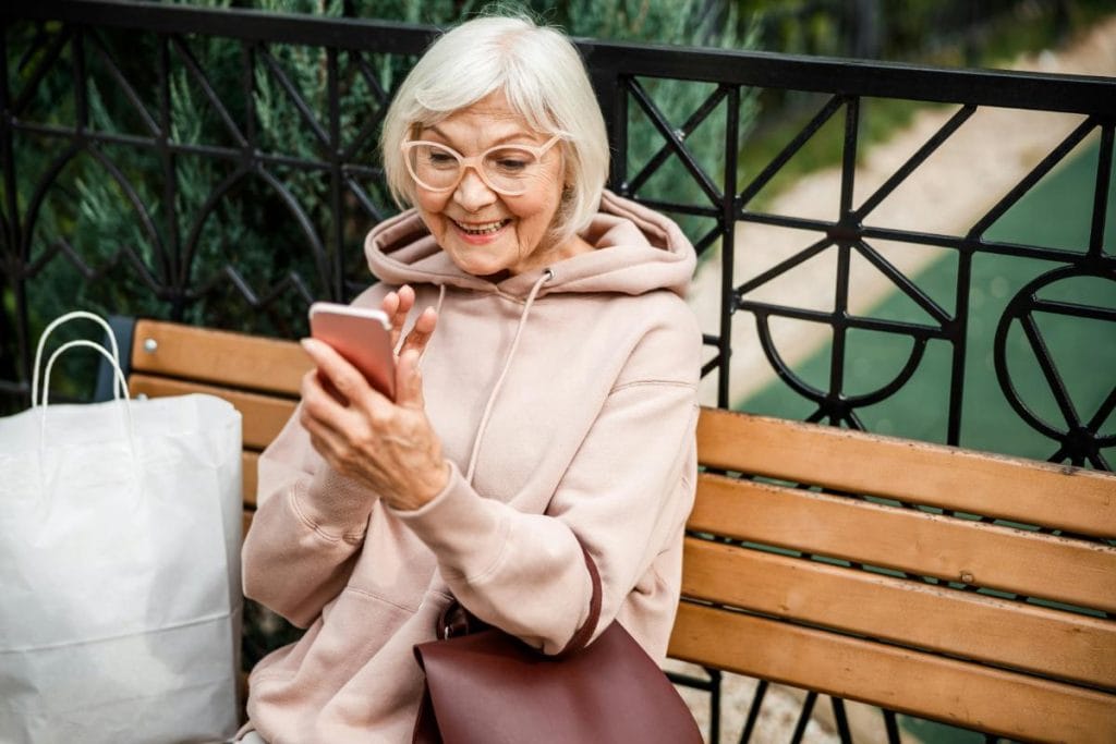 elderly woman on park bench using a smartphone