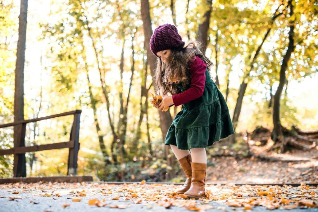 girl picking autumn leaves up off the ground