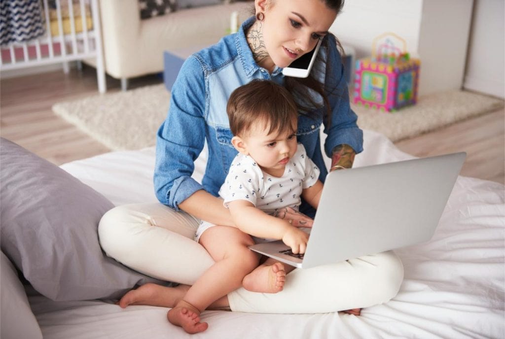 woman holding baby while using laptop