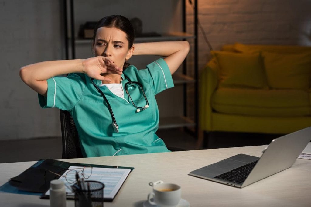 nurse sitting at a table yawning