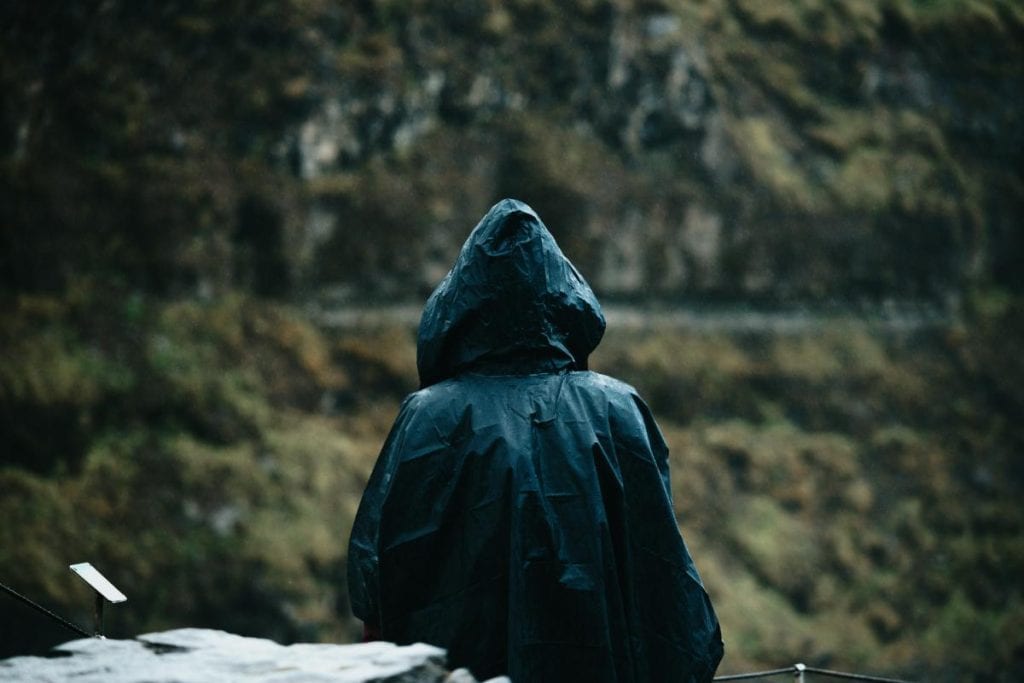 person standing in front of mountain wearing a black raincoat