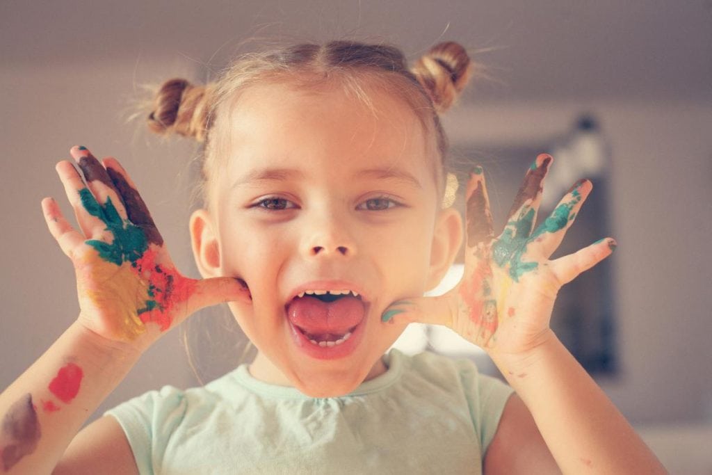 toddler girl with paint on hands making a silly face for the camera