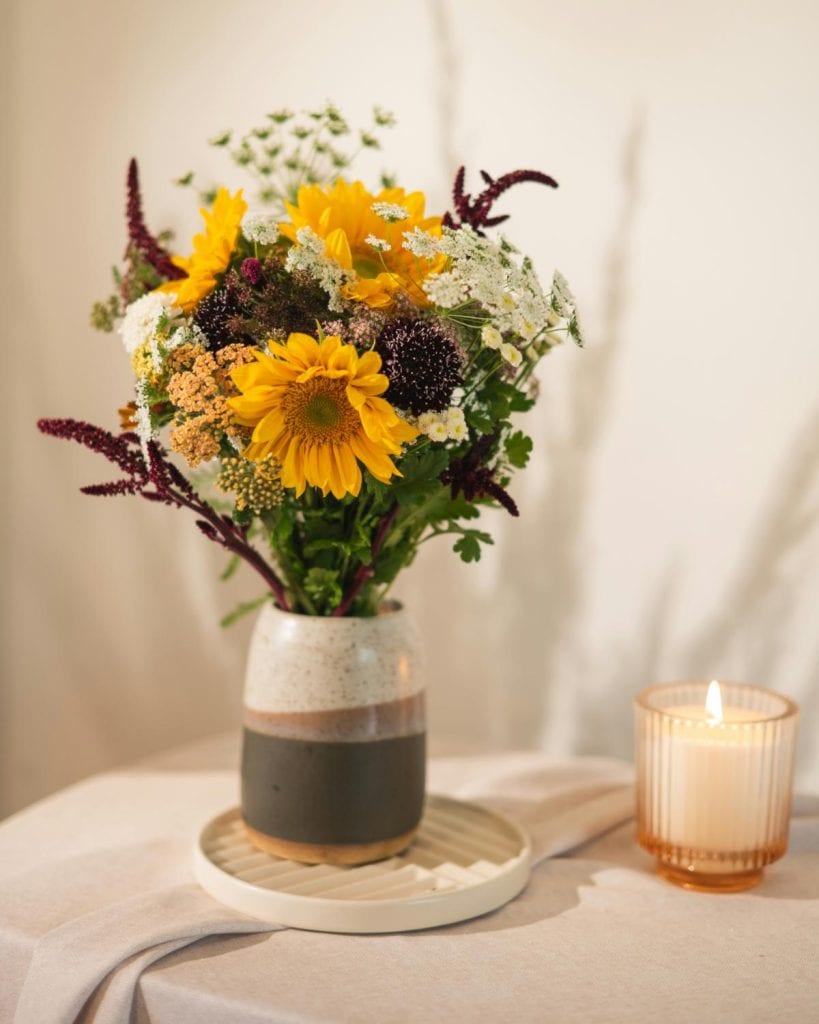 flowers in a vase on a table with a lighted candle to the right