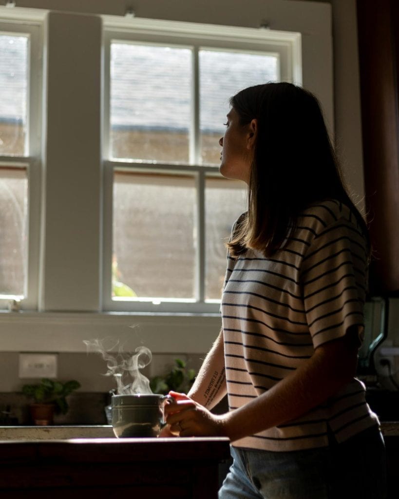 woman at sink near window with a cup of coffee