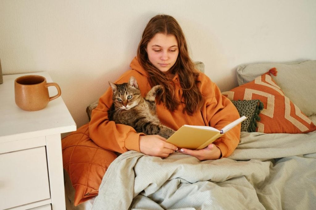 woman reading in bed while holding her cat