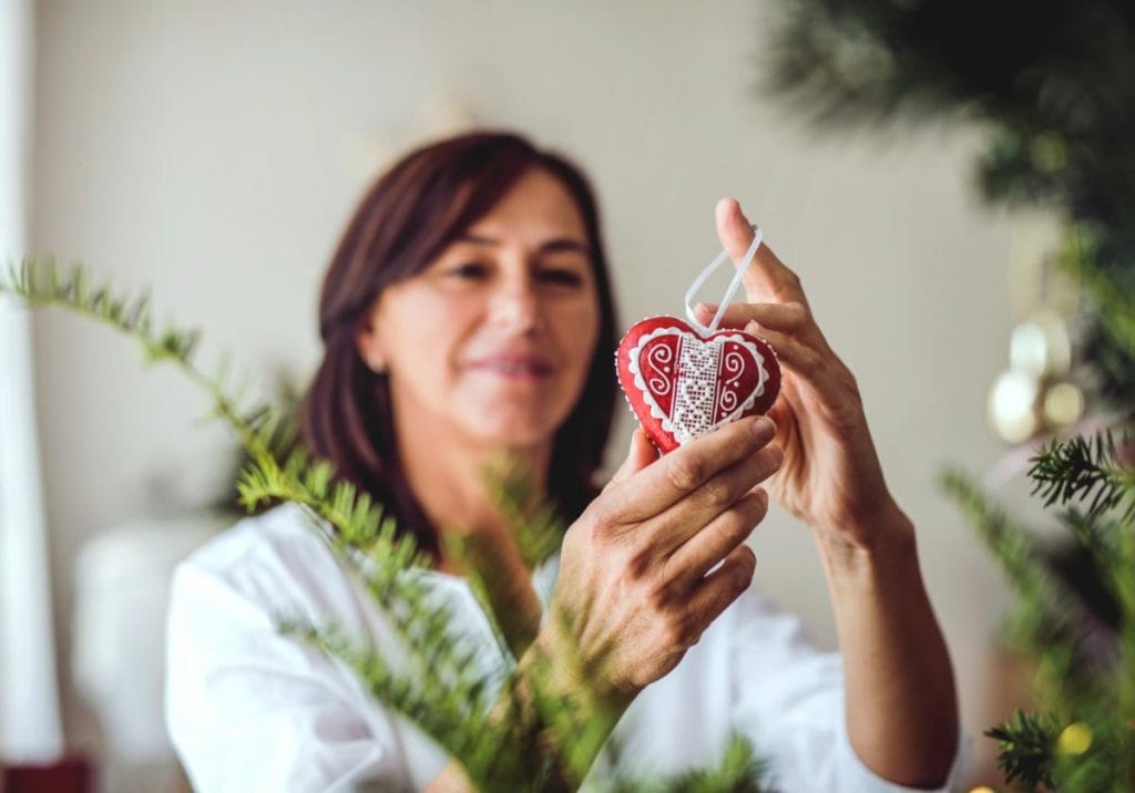 woman looking at a christmas ornament before hanging it on a tree