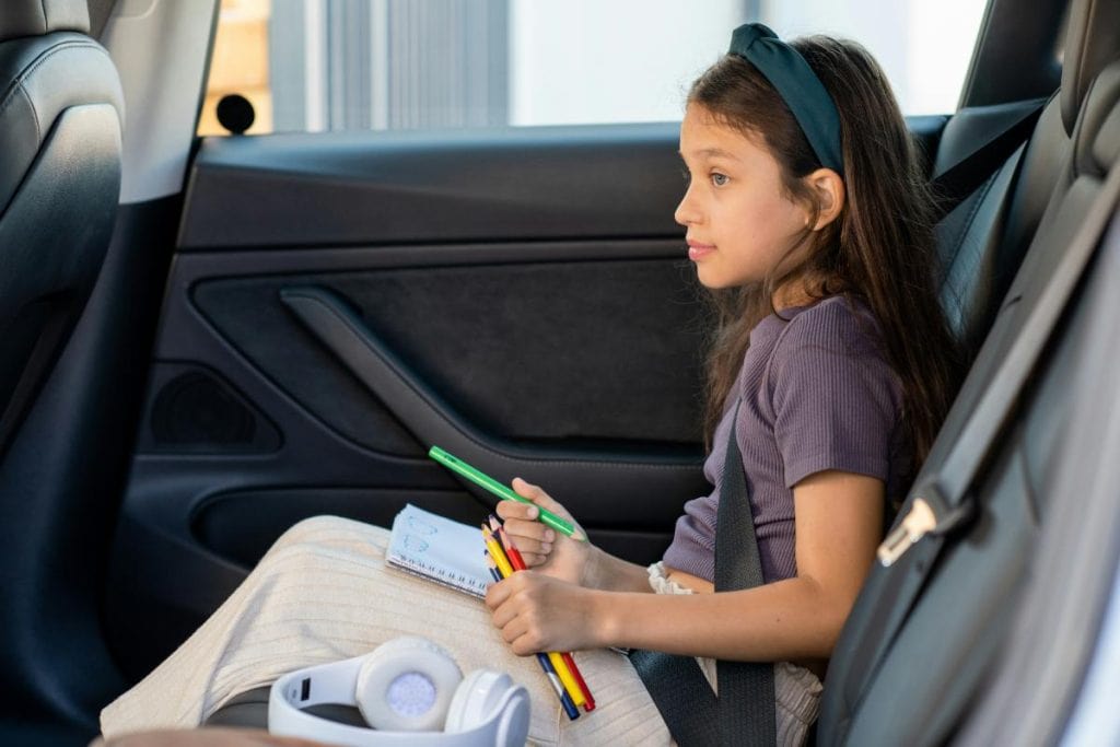 young girl with drawing materials in car