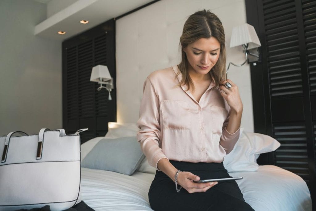 woman using tablet sitting on hotel bed