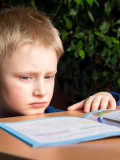 little boy who doesn't want to do his homework sitting at a desk with a booklet