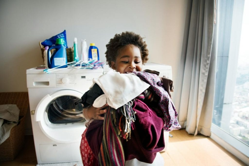 a smiling boy with an armload of laundry from the dryer