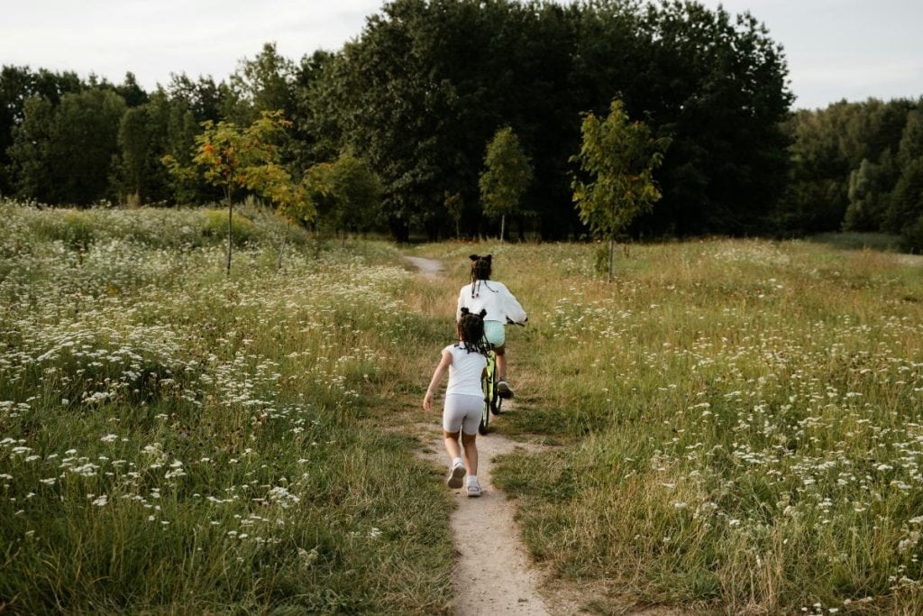 two young girls running along a dirt path through a field of wildflowers