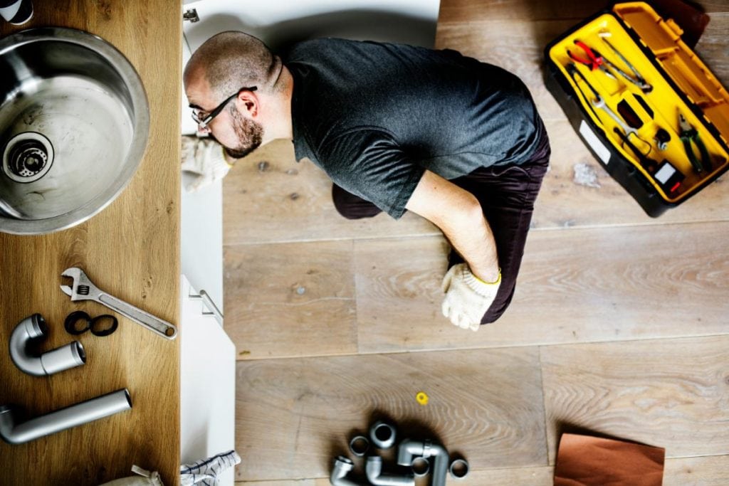 a man sitting in the floor looking at the pipes under the sink