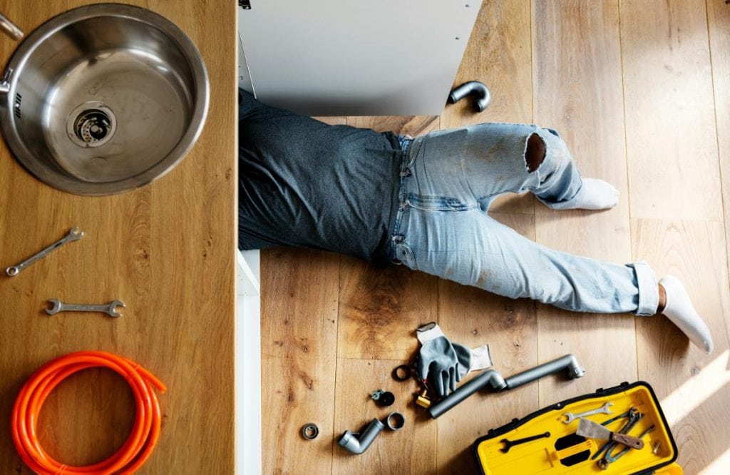 man underneath sink to work on the pipes