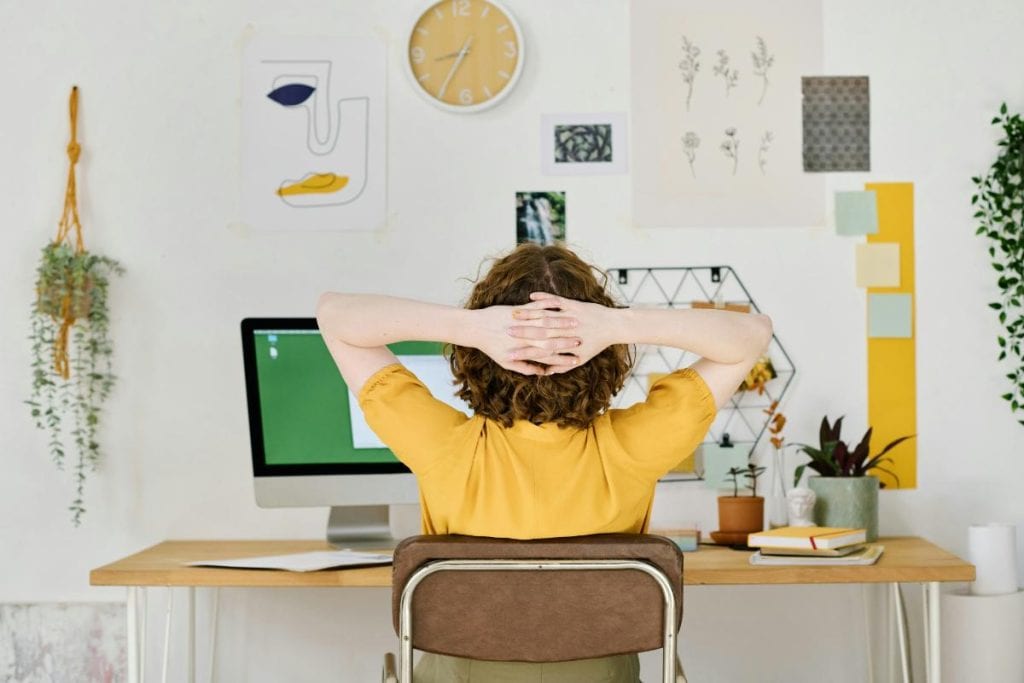 woman in home office sitting at desk with hands behind head