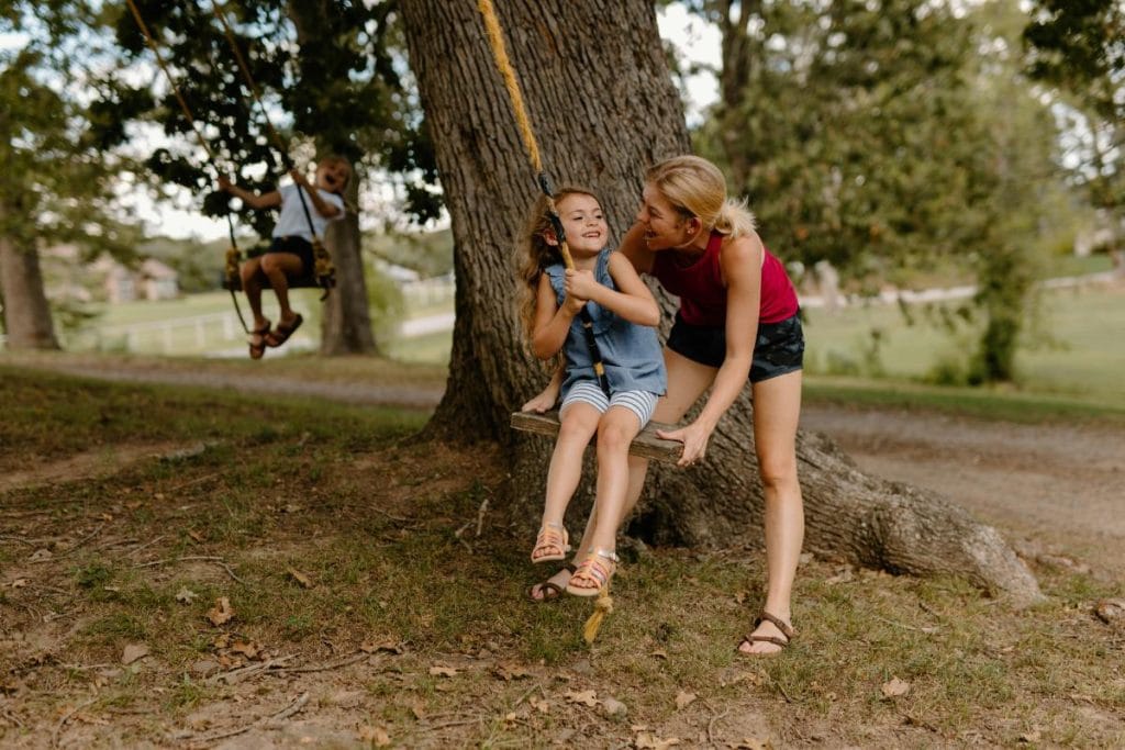 mother pushing daughter on tree swing