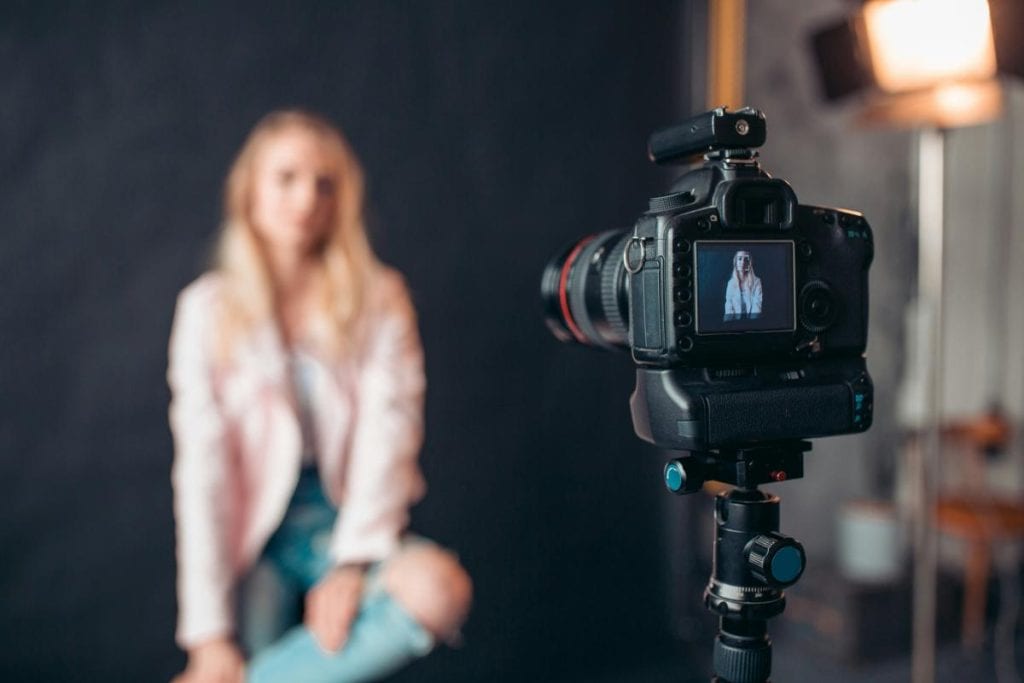 woman sitting in front of background with camera pointed toward her to take her portrait