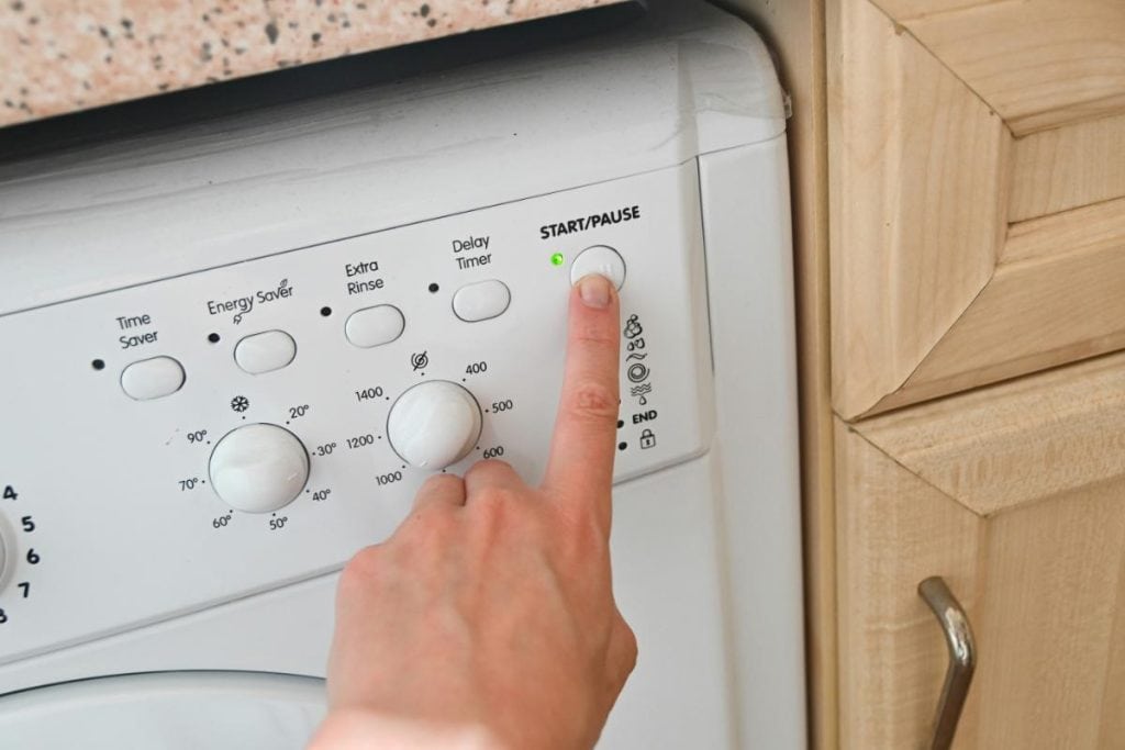 a person pushing the start button on a white dishwasher