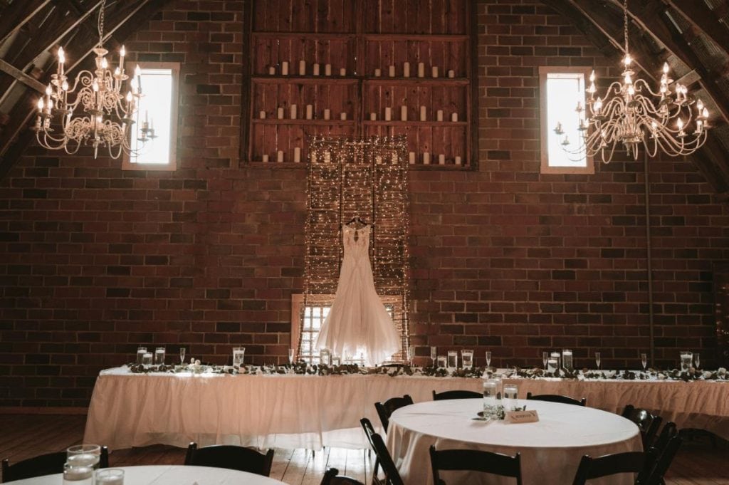 rustic wedding reception hall featuring wedding dress hanging behind the main table