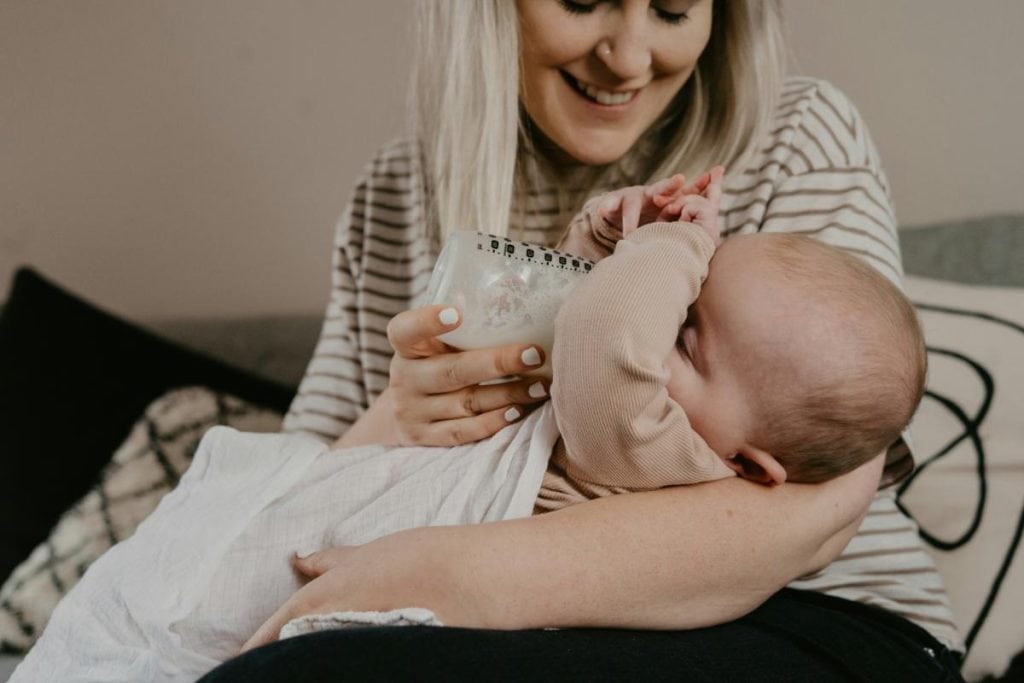 smiling mother holding baby in her arms while feeding baby a bottle