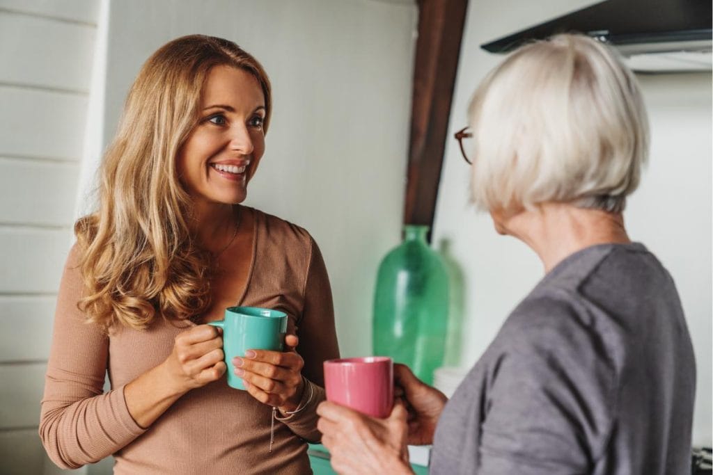 blonde woman and senior mother standing and drinking coffee