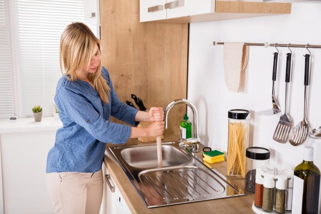 woman clearing drain with plunger