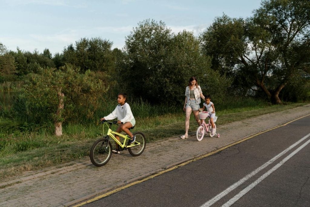 a woman walking with two girls riding bicycles along the road