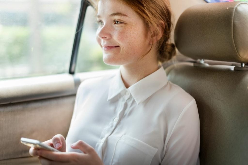 young woman sitting in car with phone in her hands