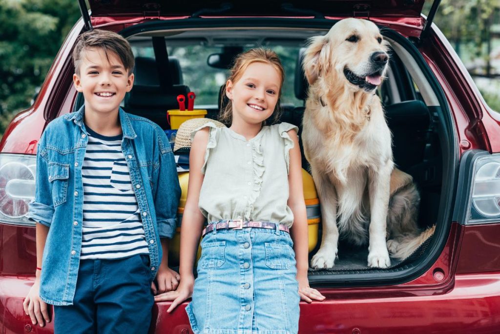 dog and two kids sitting in trunk of car for picture while traveling