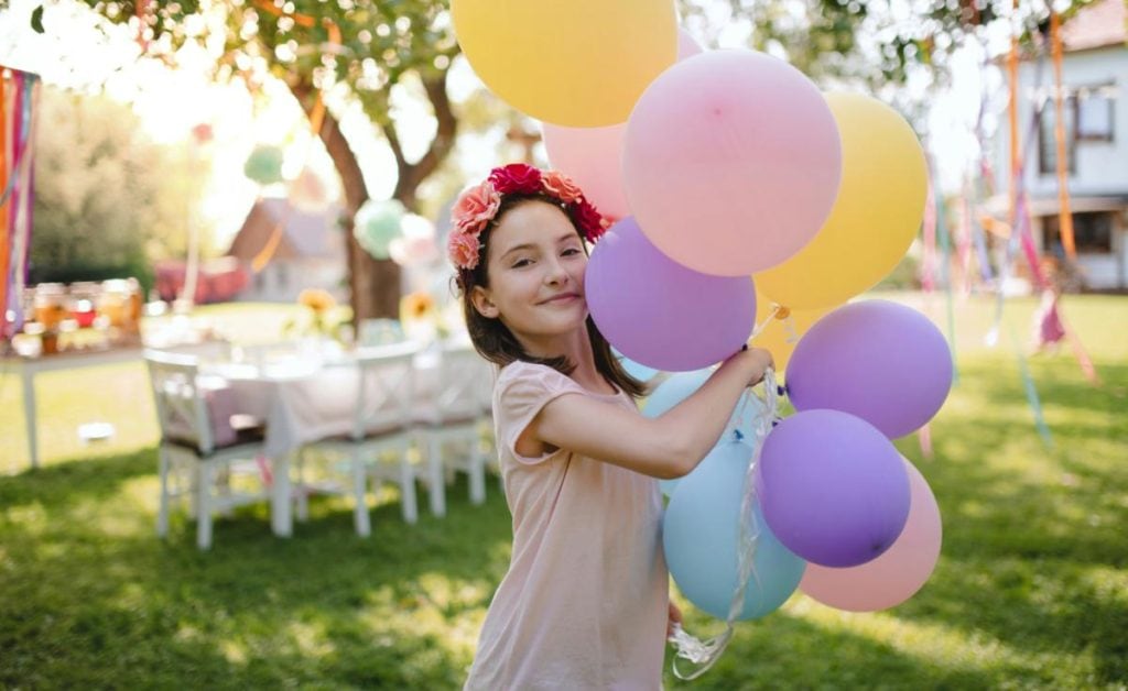 girl at outdoor summer birthday party holding colorful balloons in pastel colors