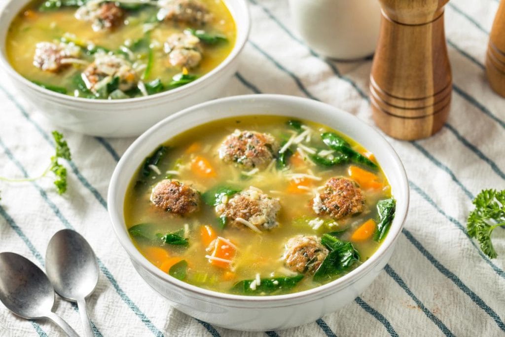 Italian wedding soup in white bowls on striped tablecloth