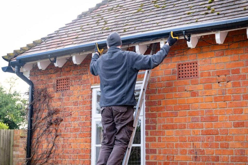 man repairing gutters on brick house